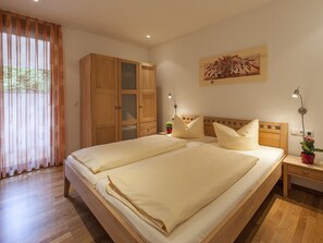A double bed with two pillows, a wooden wardrobe, a bedside table with a lamp, and a potted plant.