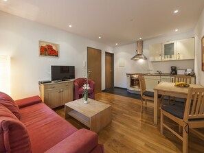 A modern living room with a sofa, a coffee table, a TV, and a dining area with a table and chairs.