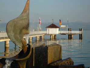 Une jetée s’avançant dans une étendue d’eau calme, avec une sculpture métallique au premier plan.