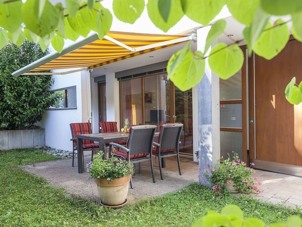 An outdoor patio with a table and chairs, a potted plant, and a glass door leading to an interior space.
