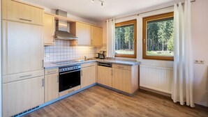 Une cuisine moderne avec des meubles en bois, un four encastré et une fenêtre donnant sur la forêt.