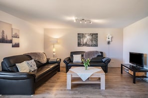 A living room with two black leather sofas, a white coffee table, a TV on a stand, and wall-mounted artwork.
