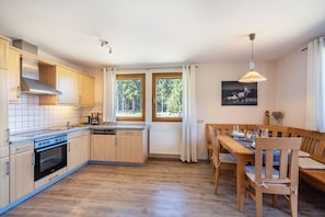 A modern kitchen with wooden cabinets, a built-in oven, and a dining area with a wooden table and chairs.