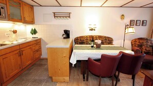 Una cocina con armarios de madera, una encimera, un fregadero, una estufa y una zona de comedor con una mesa y sillas.
