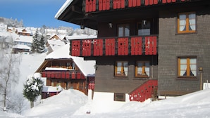 A hotel with a red balcony, snow-covered surroundings, and a view of other buildings in the background.