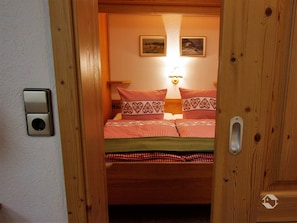 Un dormitorio con cama, una lámpara en la pared y dos cuadros enmarcados.