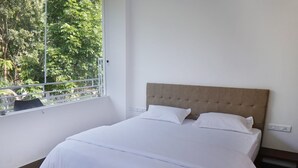 A bedroom with a large bed, white bedding, a wooden headboard, and a window with a view of greenery. - Palatty's Resort (Aluva)