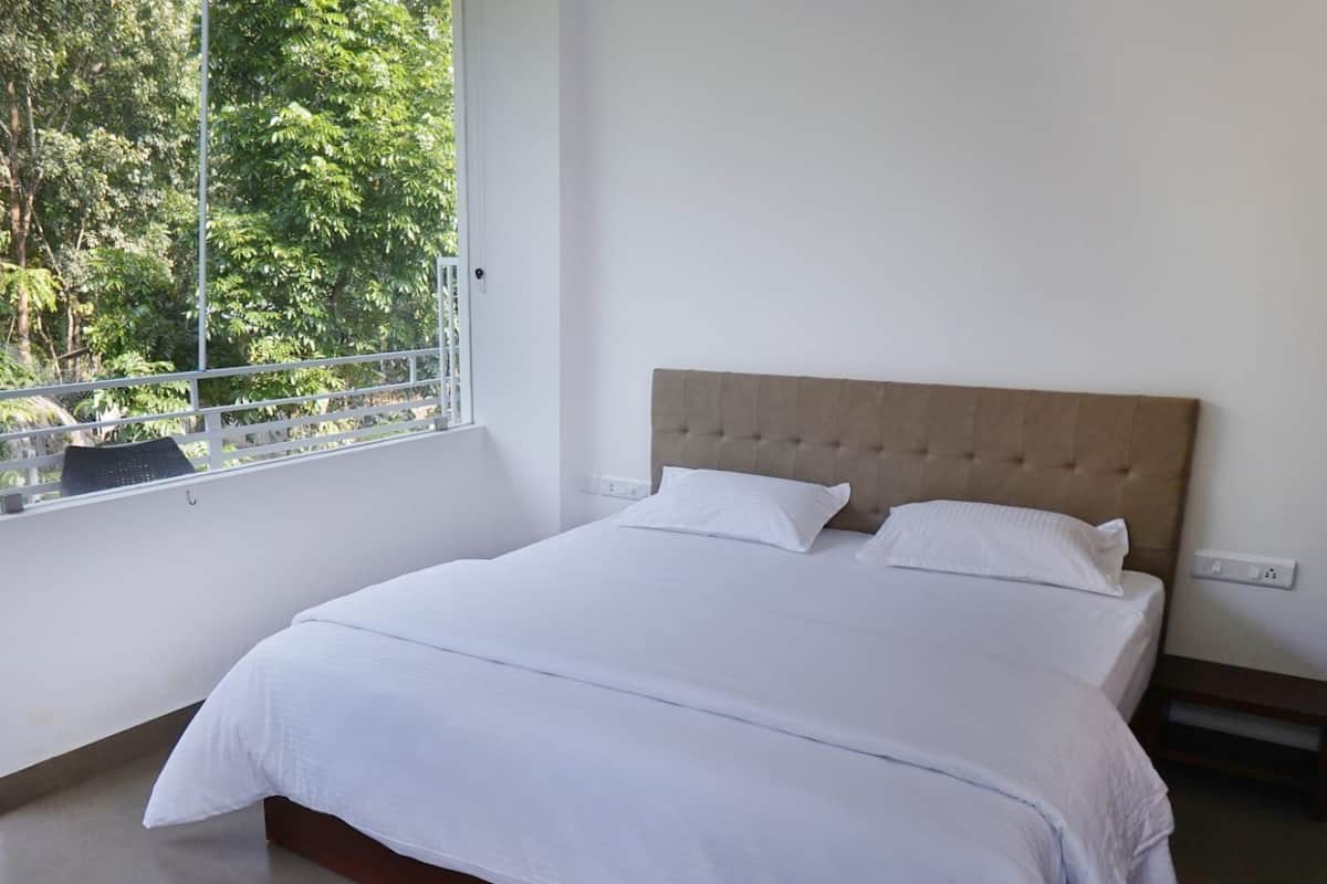 A bedroom with a large bed, white bedding, a wooden headboard, and a window with a view of greenery.