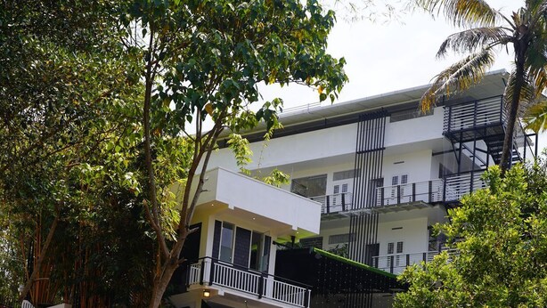 A modern building with a balcony, surrounded by lush greenery and a flowing water feature. - Palatty's Resort (Aluva)