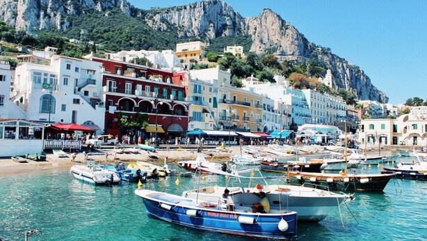 A coastal town with colorful buildings, a marina with boats, and a mountainous backdrop.
