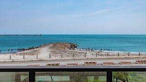 Ein Küstenblick mit felsiger Küstenlinie, einem Pier im Hintergrund und einer Reihe Bänken entlang der Promenade.