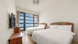 Ein Hotelzimmer mit zwei Betten, einem Fernseher, einem Nachttisch aus Holz und einem großen Fenster mit Blick auf das Meer.