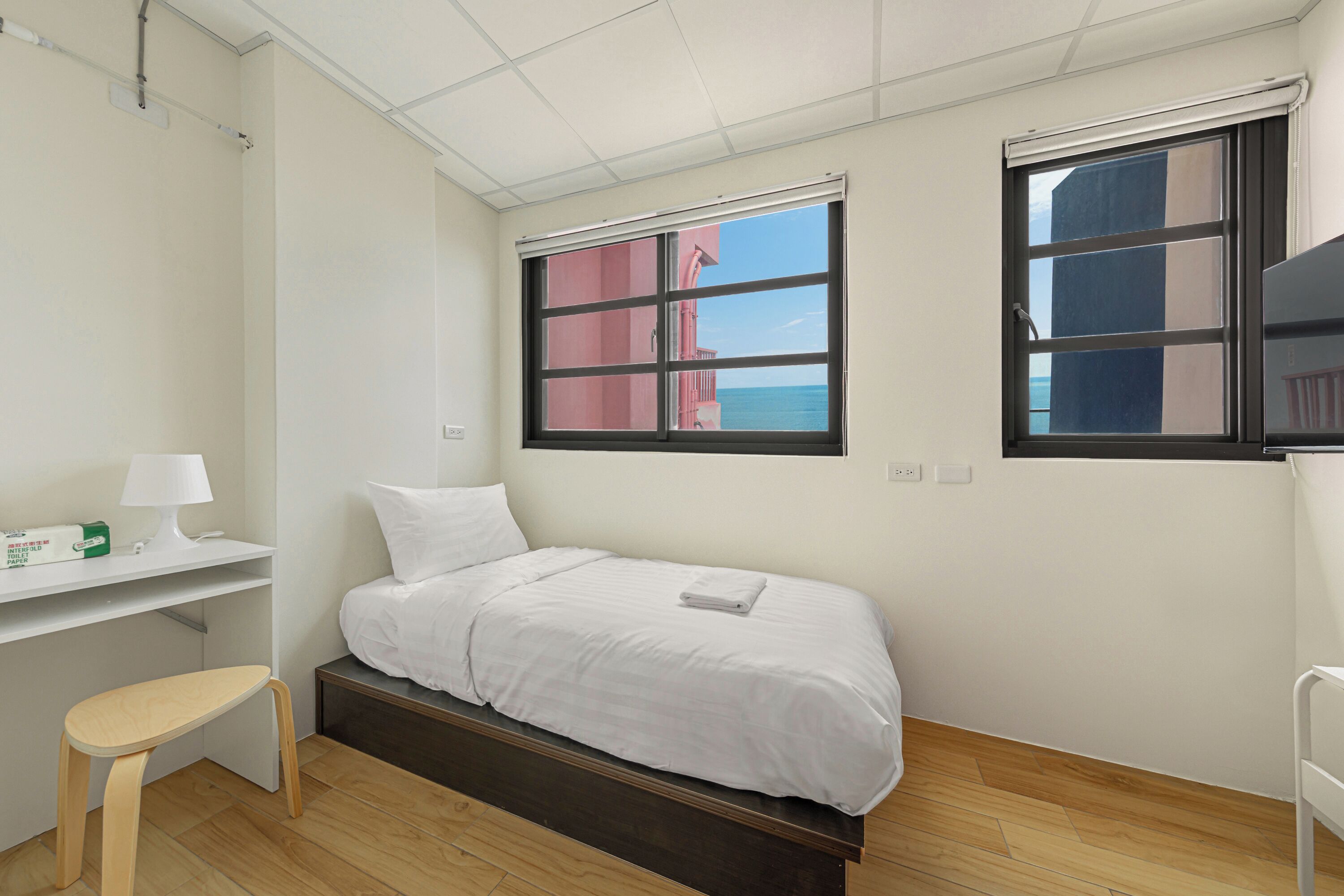 Una habitación pequeña y limpia con cama, escritorio y ventana con vista al mar.