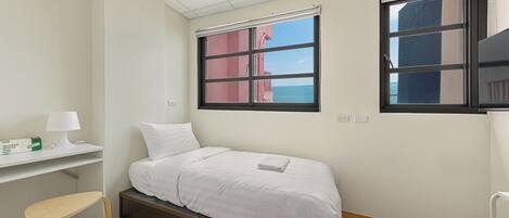 Una habitación pequeña y limpia con cama, escritorio y ventana con vista al mar.