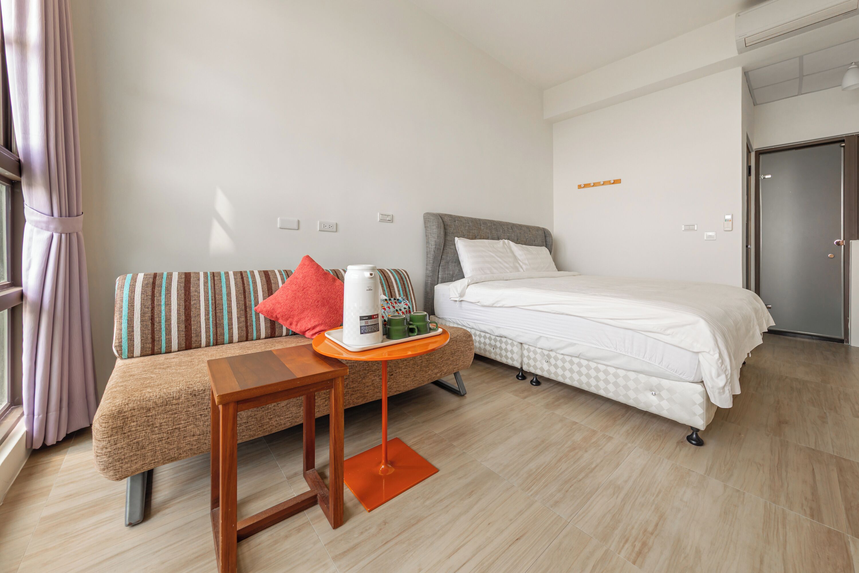 Ein Hotelzimmer mit einem Bett, einem Sofa, einem kleinen Tisch mit Kaffeemaschine und einem Fenster mit Vorhängen.