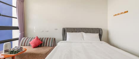 A hotel room with a large bed, a smaller sofa, a table with a coffee maker, and a window with curtains.
