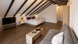 Ein modernes Loft-Schlafzimmer mit schrägem Dach, einem Bett, einem Fernseher, einem Nachttisch und einer Couch.