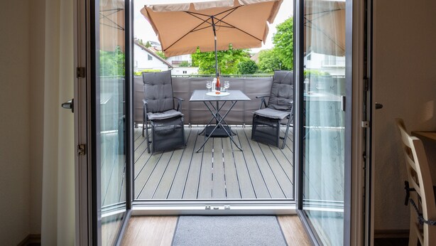 Eine Glastür führt zu einer Terrasse mit Tisch, zwei Stühlen und einem großen Sonnenschirm.
