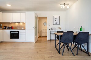 Una cocina moderna con armarios blancos, horno empotrado y comedor con mesa y sillas.