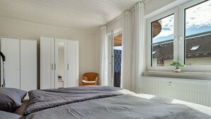 A bedroom with two beds, a window with a view, a chair, and a wardrobe. - Apartment 'Bodenseenest' with Mountain View, Balcony and Wi-Fi (Meckenbeuren)
