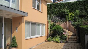 A modern house with a paved driveway, a small garden with various plants, and a staircase leading to a roof terrace. - Apartment 'Lotte Und Helmut Klanner' with Shared Terrace, Shared Garden and Wi-Fi (Daisendorf)