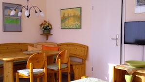 A room with a bed, a wooden dining table with chairs, a television, and artwork on the walls. - Apartment 'Lotte Und Helmut Klanner' with Shared Terrace, Shared Garden and Wi-Fi (Daisendorf)