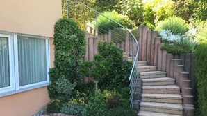A staircase with a metal handrail, surrounded by greenery and a wooden fence. - Apartment 'Lotte Und Helmut Klanner' with Shared Terrace, Shared Garden and Wi-Fi (Daisendorf)