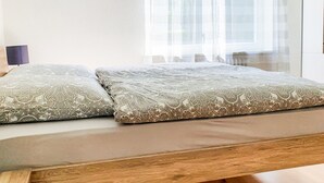 Una habitación con cama, suelo de madera y ventana con cortinas translúcidas.