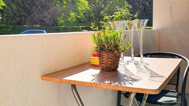 Un balcón con mesa, sillas, una planta en maceta y barandilla de vidrio.