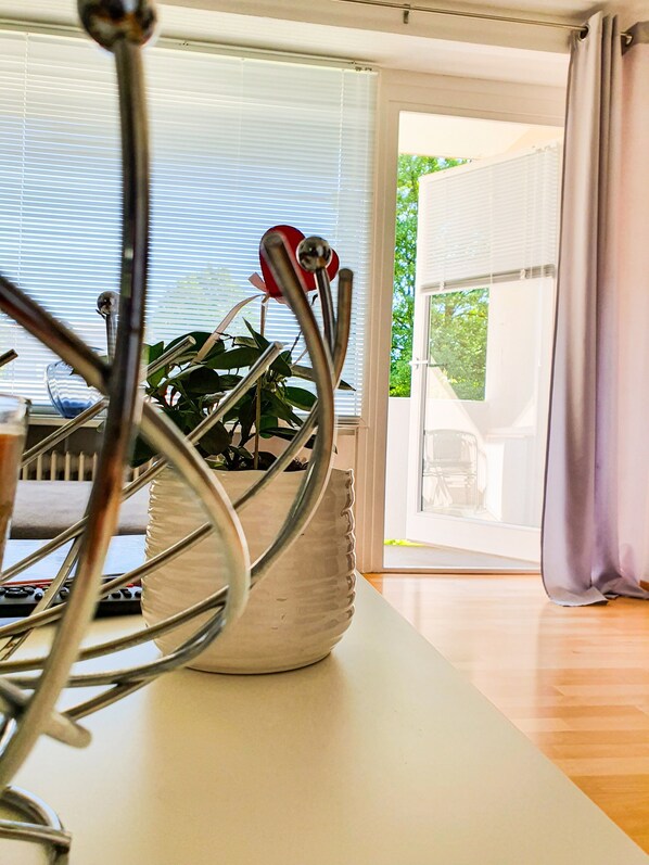 Un interior moderno con una mesa blanca, una escultura de metal, una planta en maceta y vistas a través de un ventanal.