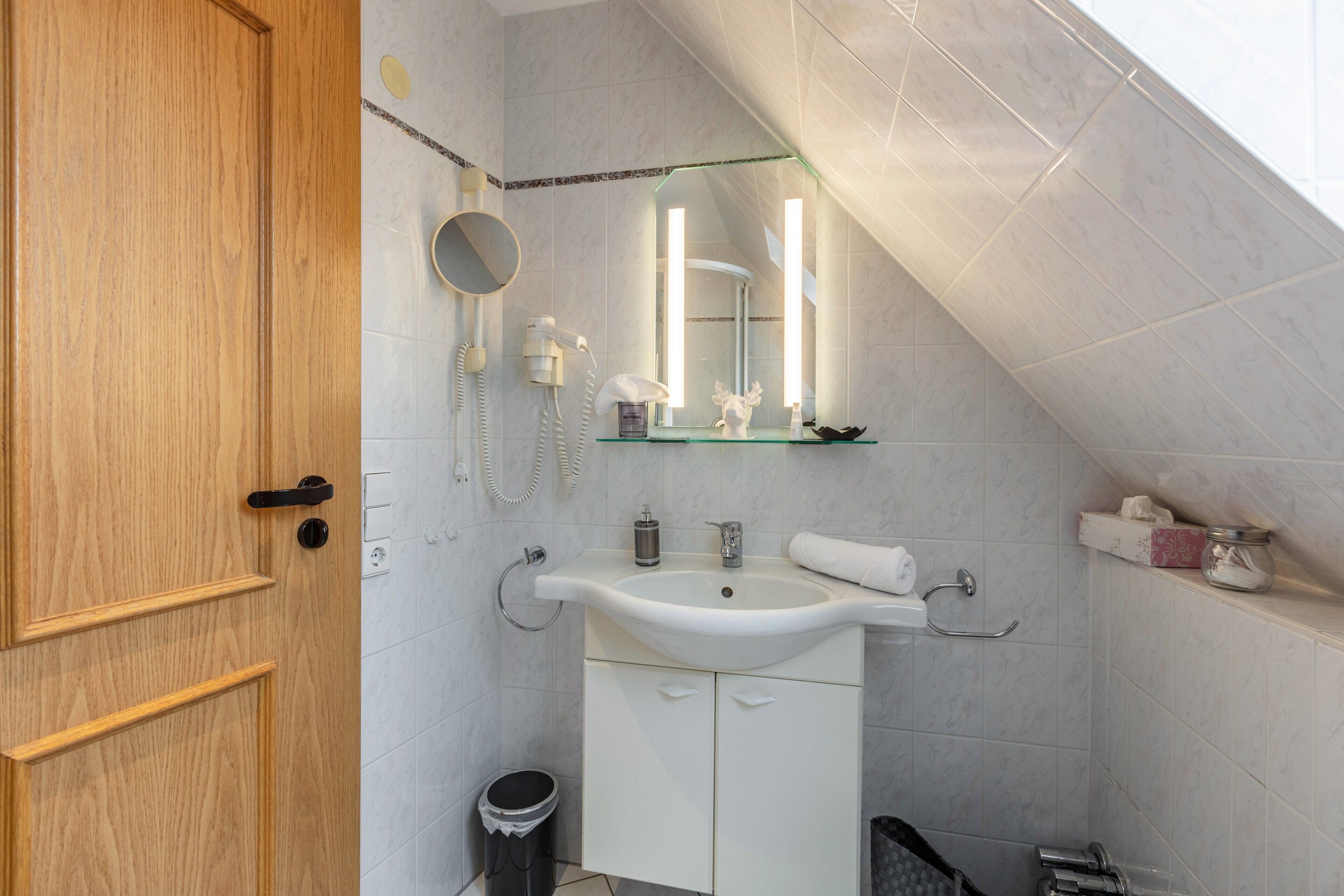 Un baño con puerta de madera, un lavabo blanco, un espejo y una zona de ducha.