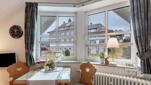 A corner room with a bay window, a table with chairs, a clock, and a view of buildings. - Apartment 'Studio' with Wi-Fi (Schluchsee)