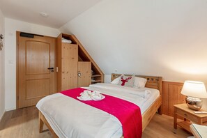 A bedroom with a bed, a nightstand, a wooden wardrobe, and a sloped ceiling.