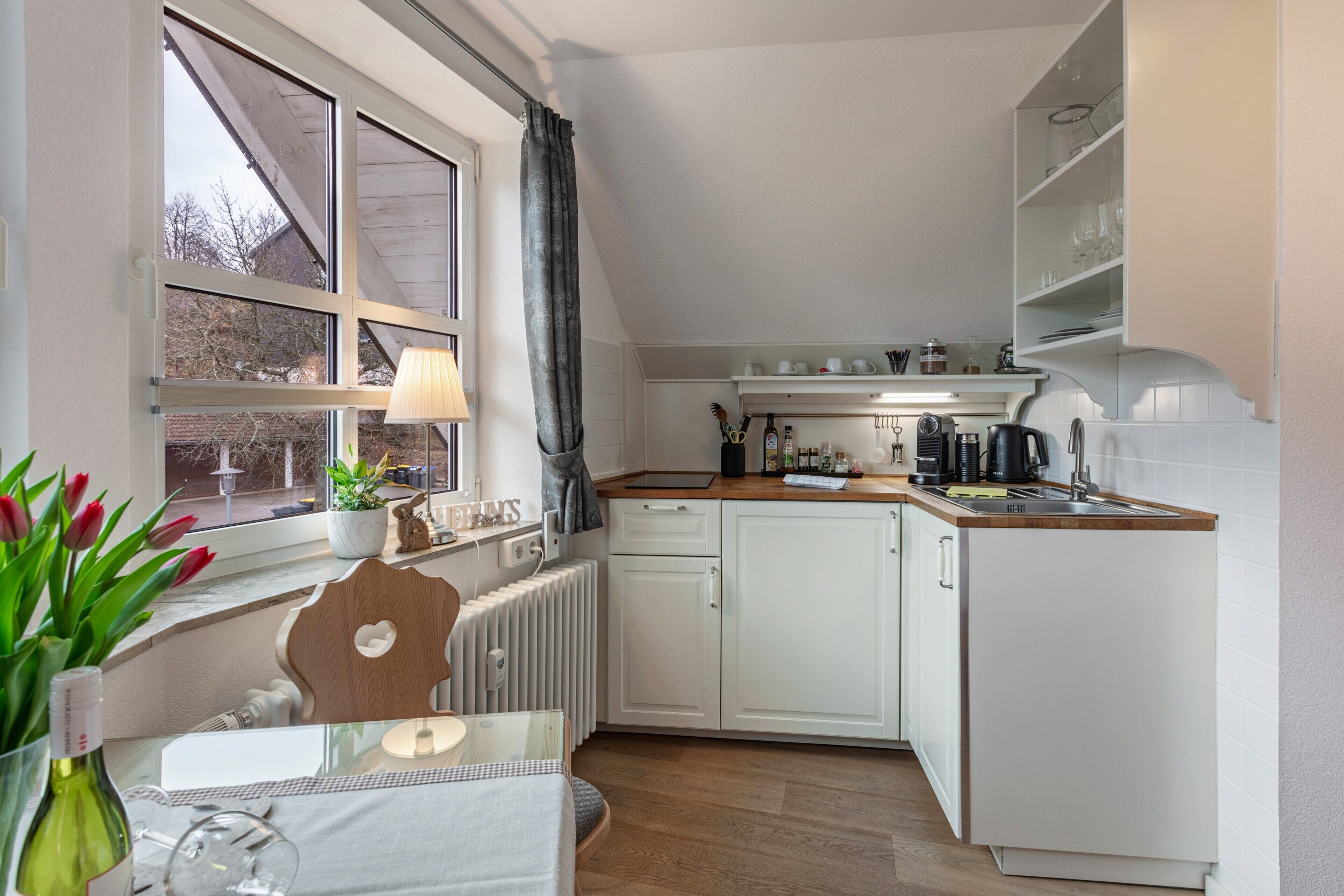 A modern kitchen with white cabinets, a wooden countertop, and a window with a view.
