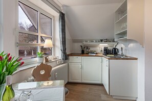 A modern kitchen with white cabinets, a wooden countertop, and a window with a view.