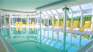 An indoor swimming pool with clear glass walls, yellow lounge chairs, and a view of a forested area. - Apartment 'Studio' with Wi-Fi (Schluchsee)