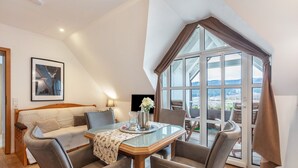 Una habitación moderna con una mesa de comedor de cristal, un sofá y un amplio ventanal con cortinas.