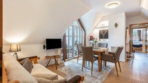 Una habitación moderna estilo loft con un ventanal grande, un televisor de pantalla plana, una zona de comedor con sillas y un rincón de descanso acogedor con un sofá y almohadas.