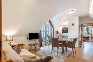 A modern loft-style room with a large window, a flat-screen TV, a dining area with chairs, and a cozy seating area with a sofa and pillows. - Apartment 'Seaview' with Shared Garden, Balcony and Wi-Fi (Schluchsee)