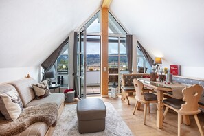 A loft-style room with a dining area, a sofa with deer pillows, a fur throw, and a view of the outdoors. - Holiday Apartment 'Seaside' with Balcony and Wi-Fi (Schluchsee)