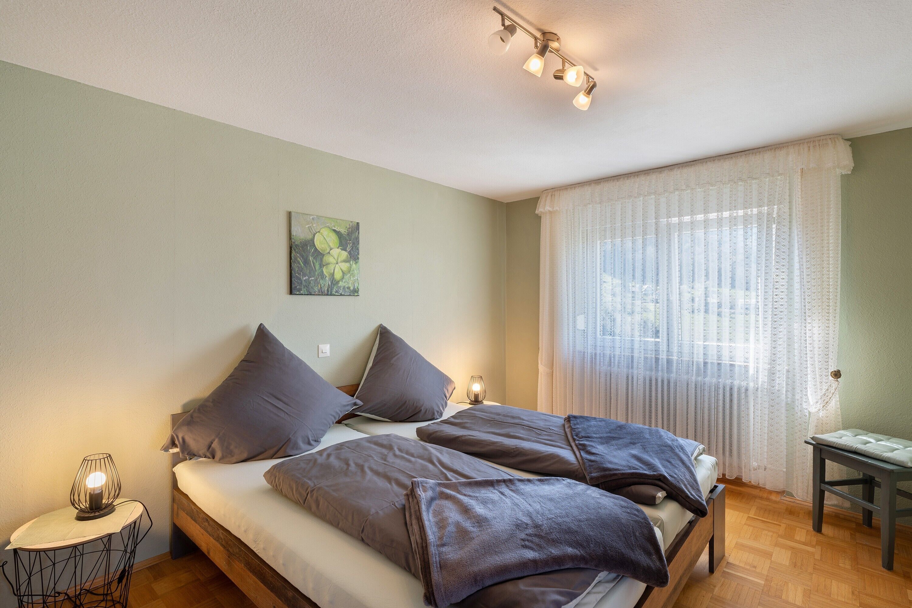 Un dormitorio con cama, mesita de noche, lámpara y ventana con cortinas.