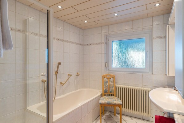 Et badeværelse med bruseniche, en træstol, en radiator og et vindue.