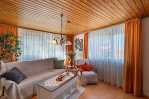 A living room with a wooden ceiling, a sofa, a chair, a coffee table, and a large window with curtains. - Apartment 'Ferienwohnung Gabriele' with Mountain View, Private Terrace and Wi-Fi (Lauf)
