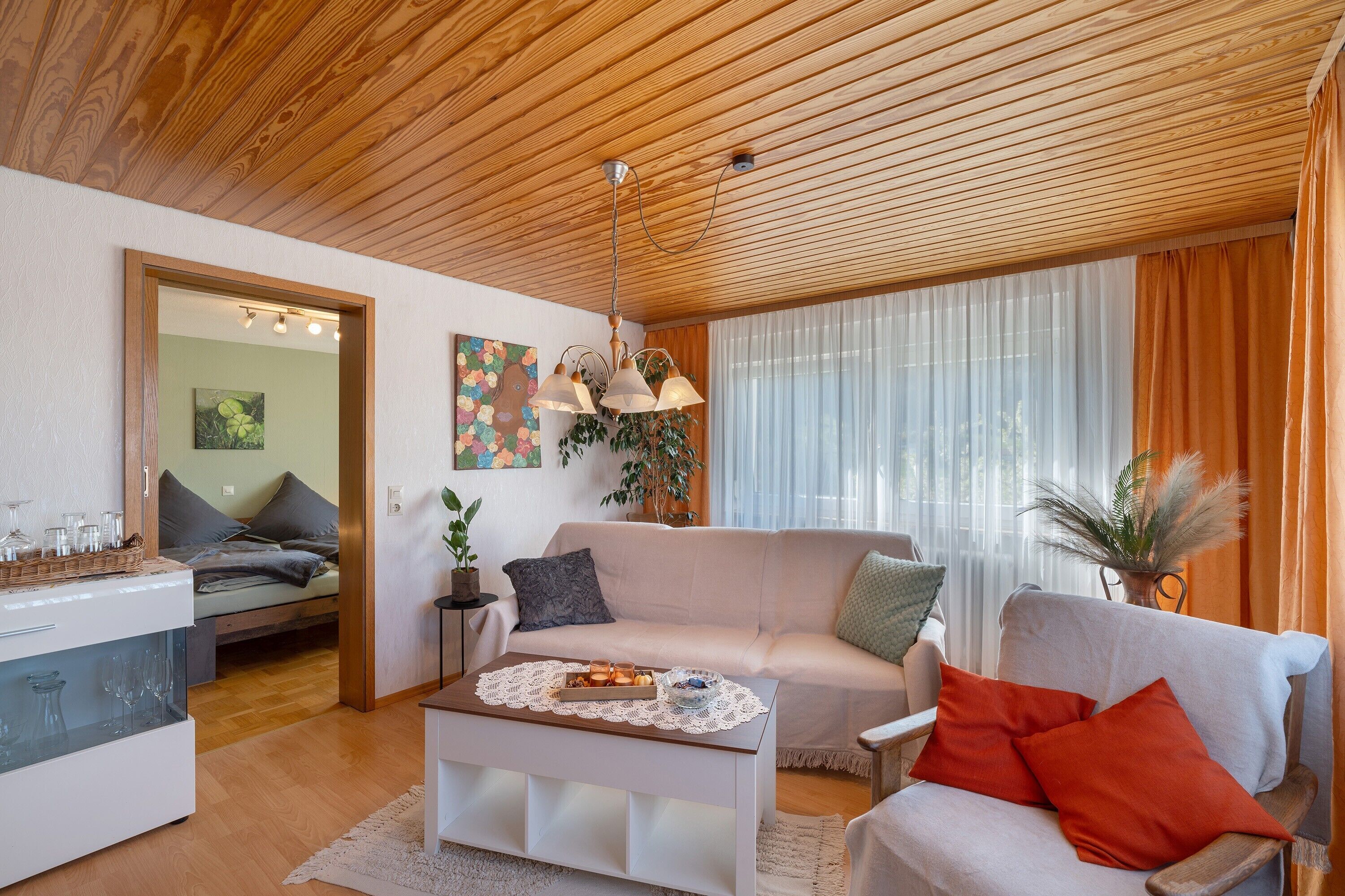 A modern living room with a wooden ceiling, a white sofa, a coffee table with a tray of snacks, and a side table with a vase.