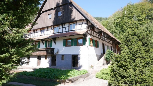 A traditional half-timbered house with a sloped roof, a balcony, and a garden area.
