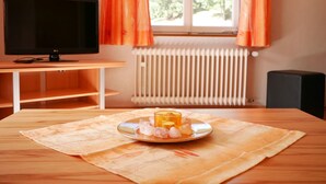 A room with a television, a table with a plate of food, a window with curtains, and a radiator.