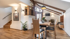 A modern interior with a wooden staircase, a dining area with a table and chairs, and a cozy seating area with a bench. - Chalet 'Hochsitz' incl. Königscard (Gaißach)