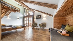 A loft-style room with a wooden ceiling, a bed, two armchairs, a sofa, and a TV mounted on the wall. - Chalet 'Hochsitz' incl. Königscard (Gaißach)