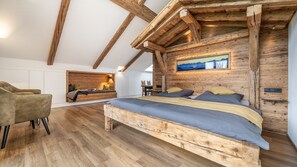 Ett sovrum med en säng i loftstil, träbjälkar, en tavla och ett skrivbord med stolar.