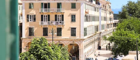 Un edificio de varios pisos con balcones, una calle al frente y coches estacionados.